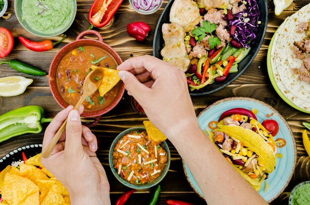 Mano sosteniendo cuchara y nacho cerca de comida mexicana