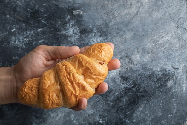 Mano sosteniendo un delicioso croissant sobre un fondo gris.