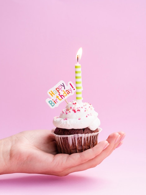 Mano sosteniendo delicioso muffin con cartel de feliz cumpleaños