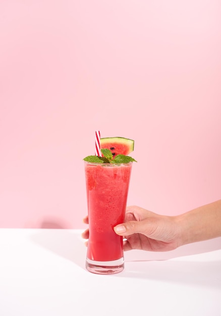 Foto gratuita mano sosteniendo jugo de sandía fresca o batido en vasos con pedazos de sandía