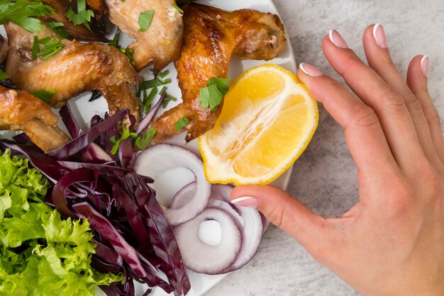 Mano sosteniendo un limón cerca de alitas de pollo