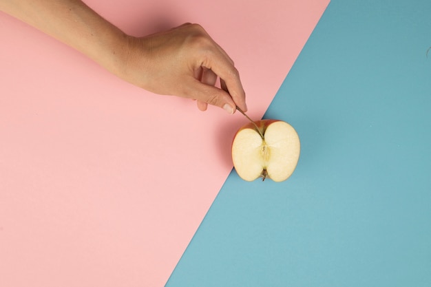 Foto gratuita mano sosteniendo una media manzana sobre fondo rosa y azul