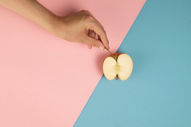 Mano sosteniendo una media manzana sobre fondo rosa y azul