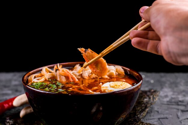 Mano sosteniendo palillos con ramen de camarones