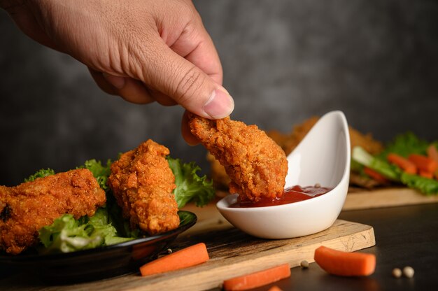 Mano sosteniendo pollo frito crujiente bañado en salsa de tomate