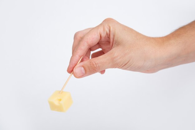 Mano sosteniendo queso cortado en cubitos con palillo de dientes