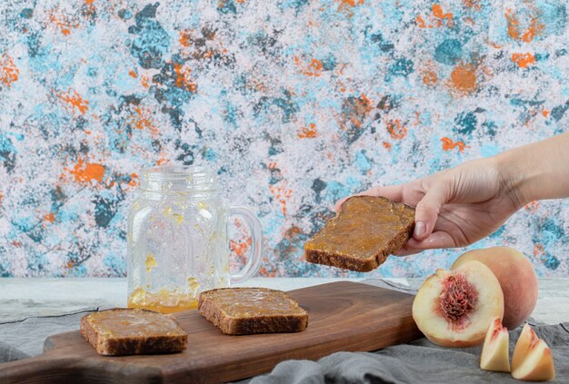 Mano sosteniendo una rebanada de pan con mermelada de melocotón.