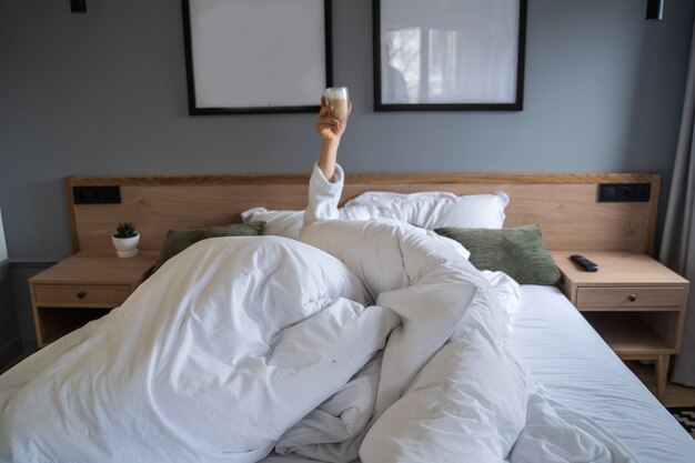 Mano sosteniendo una taza de café en su casa en la cama