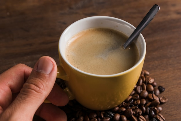 Mano sosteniendo la taza con una cuchara y café