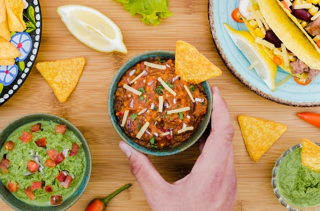 Foto gratuita mano sosteniendo una taza de guarnición con nacho cerca de comida mexicana