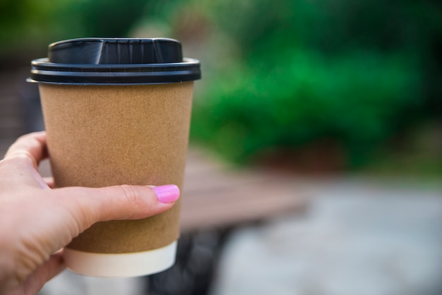 Mano sosteniendo la taza de papel de café en el fondo natural de la mañana