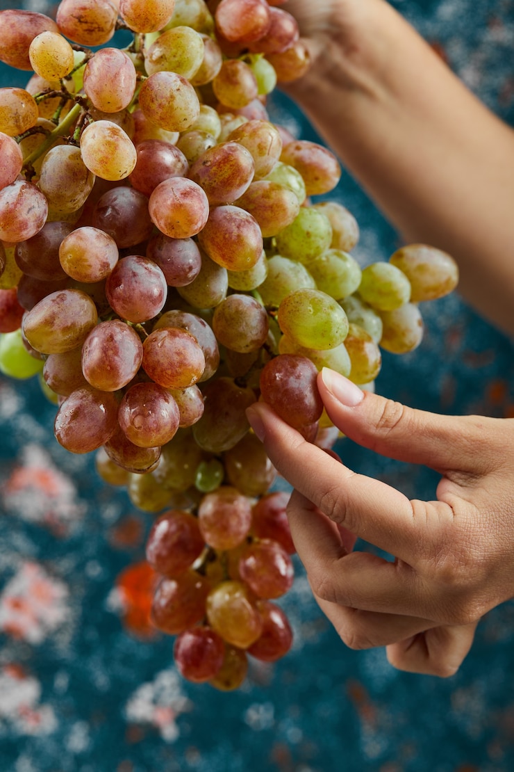 Foto gratuito mano sosteniendo uvas rojas sobre superficie azul