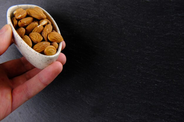 La mano sostiene un plato blanco lleno de almendras marrones sobre negro