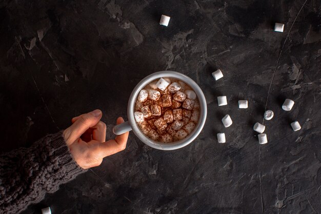 Mano sujetando chocolate caliente con malvaviscos y cacao en polvo