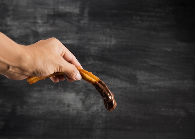 Mano sujetando un churros con chocolate y copia espacio