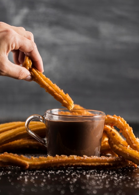 Mano sujetando un churros encima de un vaso de chocolate