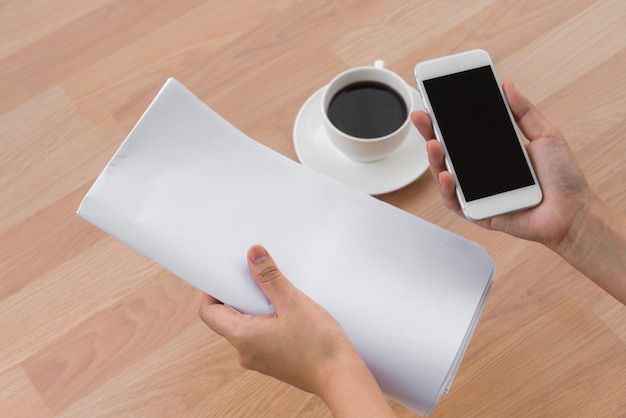 Mano sujetando una hoja de papel, un móvil y un café en la mesa