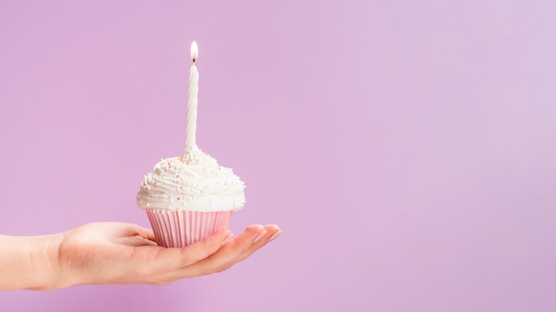 Mano sujetando muffins de cumpleaños sobre fondo rosa