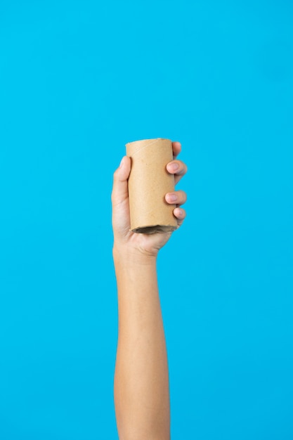 Foto gratuita mano sujetando el núcleo de papel tisú usado sobre fondo azul.