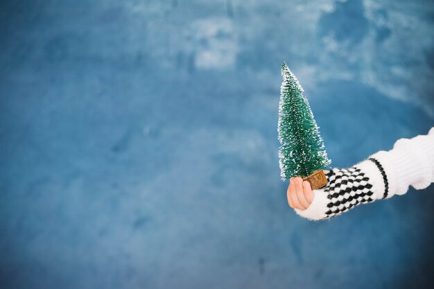 Mano sujetando pequeño árbol de navidad y espacio a la izquierda