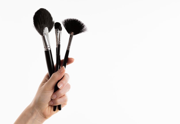 Foto gratuita mano sujetando pinceles de maquillaje con espacio de copia