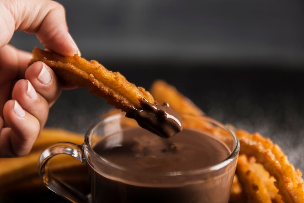 Foto gratuita mano sumergiendo un churros fritos en chocolate