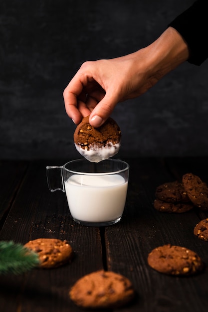 Mano sumergiendo deliciosas galletas en un vaso de leche