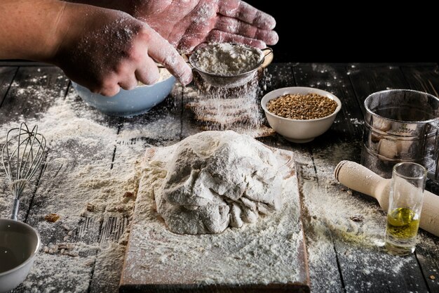 Mano tamiza la harina sobre la masa en la mesa