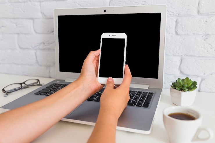 Foto gratuito mano con teléfono inteligente sobre la computadora portátil abierta