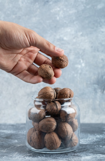 Mano tomando dos nueces de un frasco de vidrio.