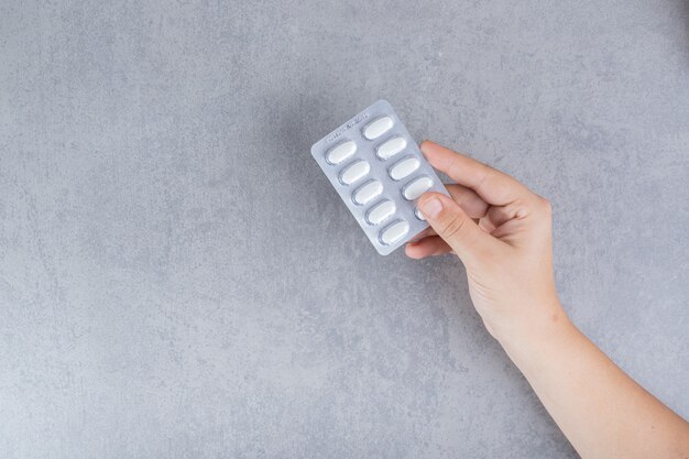 Mano tomando una pastilla blanca sobre una superficie gris