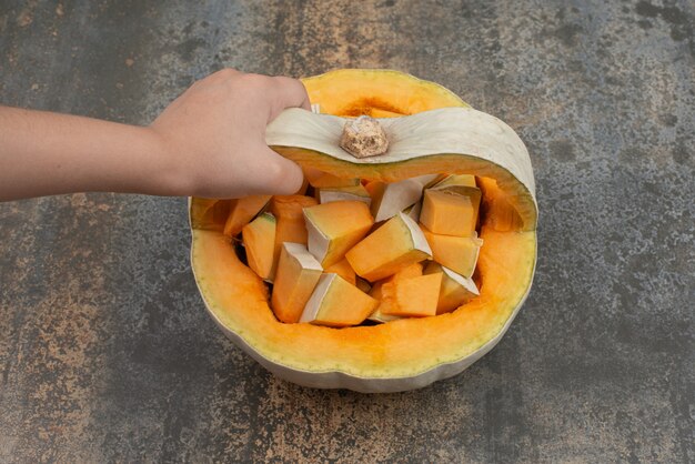 Mano tomando una rodaja de calabaza en la pared de mármol