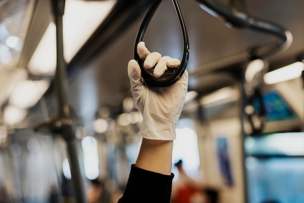 Foto gratuita mano usando un guante de látex mientras sostiene un pasamanos de tren para prevenir la contaminación por coronavirus