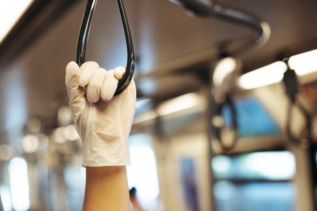 Mano usando un guante de látex mientras sostiene un pasamanos de tren para prevenir la contaminación por coronavirus