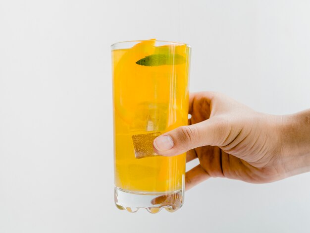 Mano con vaso de jugo de naranja frío