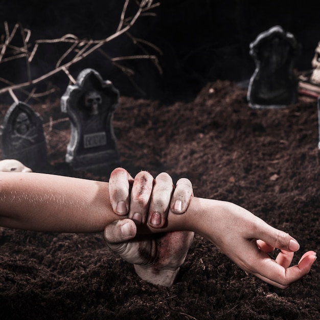 Mano de Zombie sosteniendo el brazo de la persona en el cementerio de Halloween