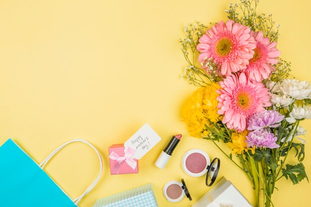 Manojo de flores frescas cerca de la etiqueta con palabras del día de la madre feliz en la caja actual y lápices labiales con polvos