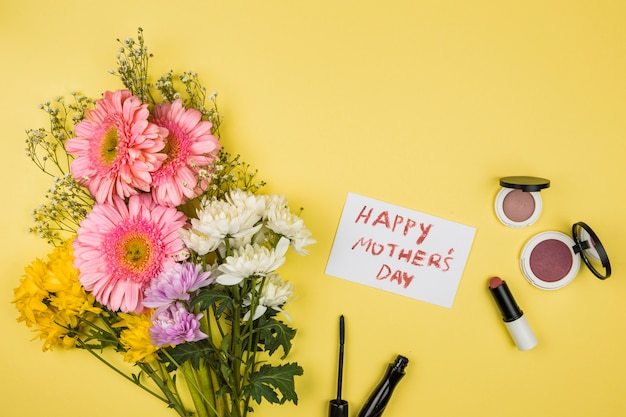 Manojo de flores frescas cerca del papel con palabras del día de la madre feliz y lápices labiales con polvos