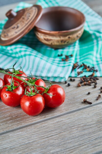 Manojo de tomates con rama y recipiente vacío con clavo de olor en la mesa de madera