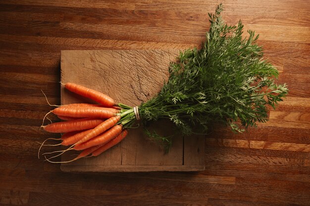 Un manojo de zanahorias frescas sobre una vieja tabla de cortar desgastada con cortes profundos en una hermosa mesa de madera marrón, vista superior