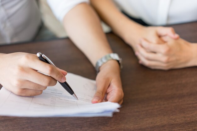 Manos del agente masculino explicando las disposiciones del contrato al cliente femenino