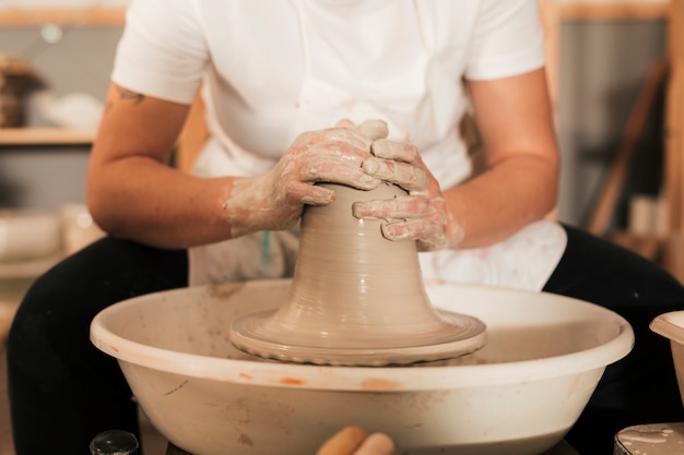 Las manos de un alfarero femenino creando un tarro de barro en la rueda de alfarería