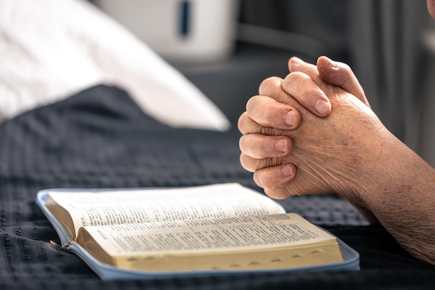 Foto gratuita las manos de una anciana dobladas en oración frente a un libro de la biblia