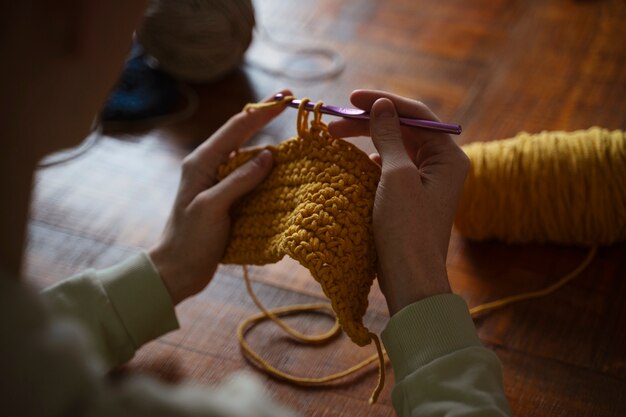 Manos de ángulo alto tejiendo con hilo amarillo.