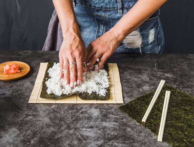 Manos arreglando ingredientes en estera de sushi