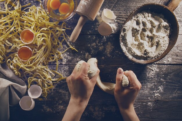 Manos de cocinero de la mujer preparando la fabricación sabrosa casera de pasta italiana clásica en la mesa de madera. De cerca. Vista superior. Viraje.