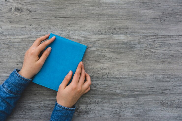 Foto gratuito manos colocando un libro con la cubierta azul