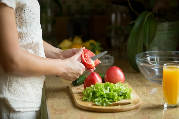 Manos cortando los tomates, ensalada en el tablero