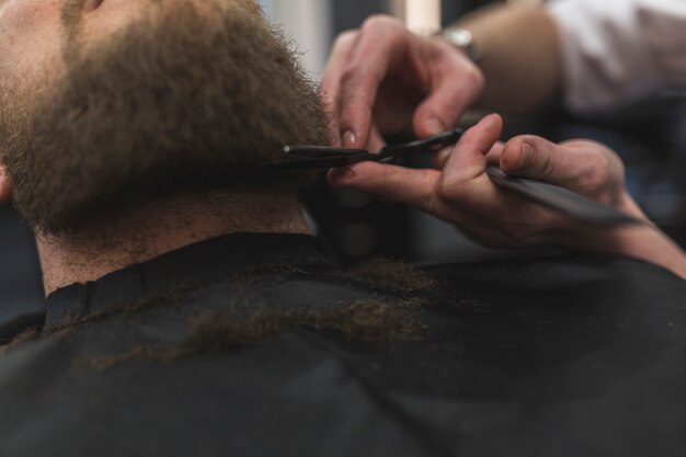 Las manos de la cosecha cortan la barba del cliente