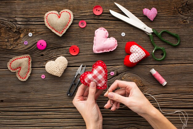 Manos cosiendo una forma de corazón rojo sobre fondo de madera